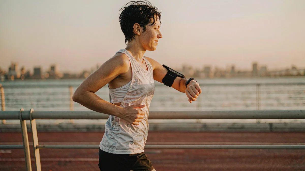 Runner checking a smartwatch on a city waterfront at sunrise