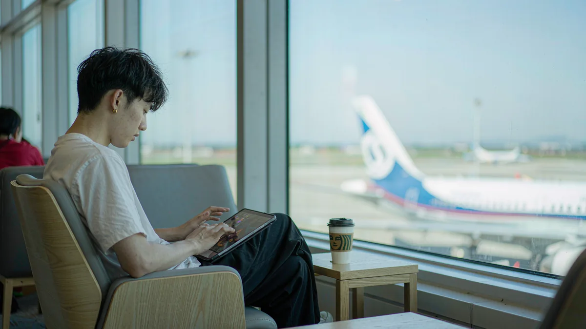 Traveler using a tablet by an airport window with an airplane outside