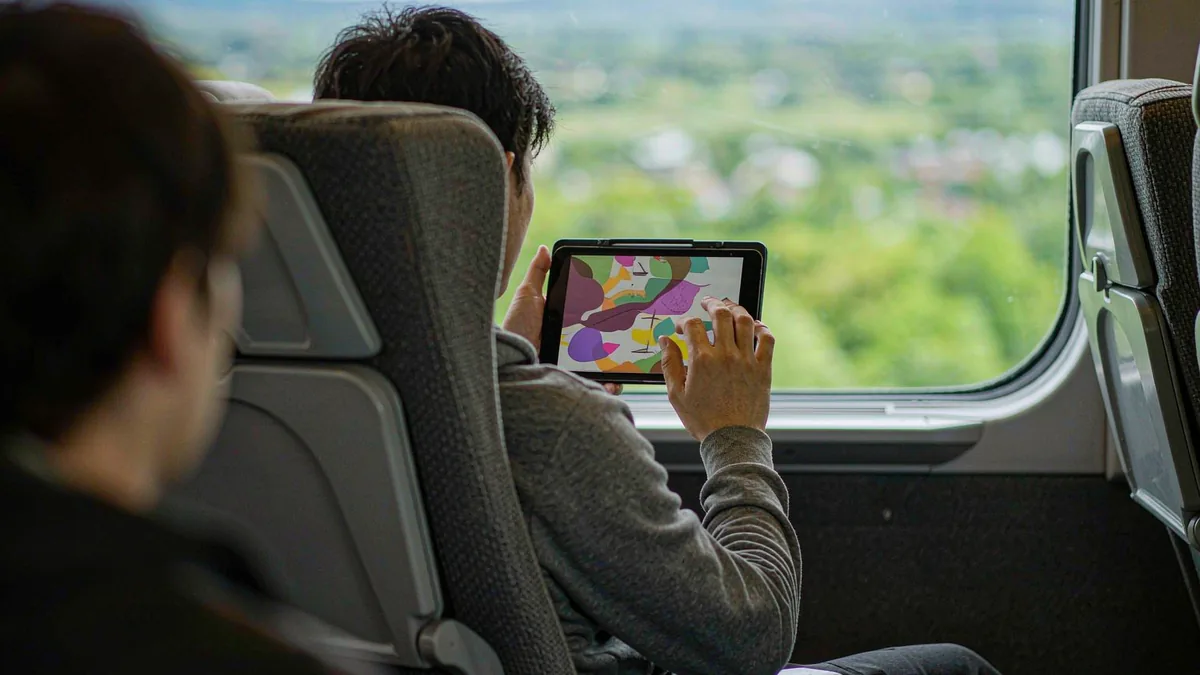 Traveler using a tablet on a train with countryside passing by