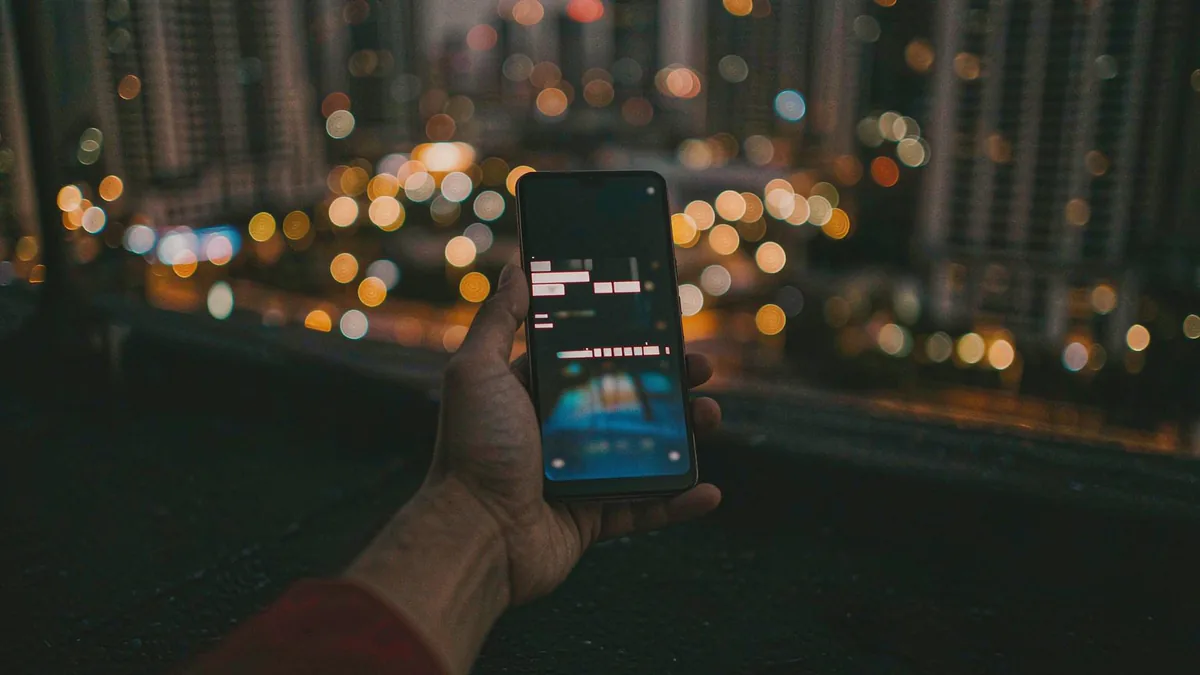 iPhone Air in hand on a hotel balcony overlooking a city at dusk